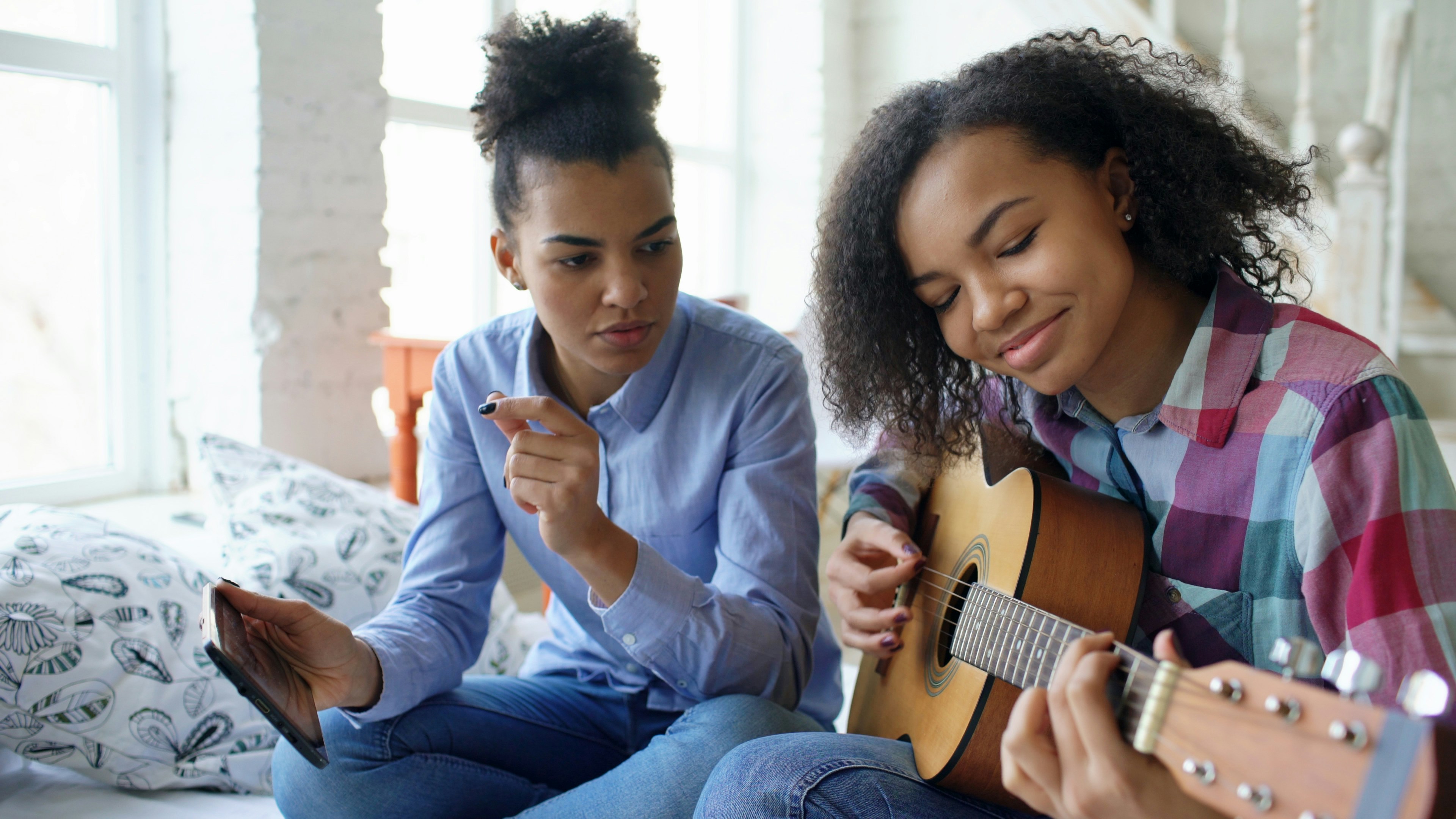 Two young women learning to play guitar together