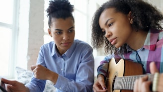 Two young women learning to play guitar together.