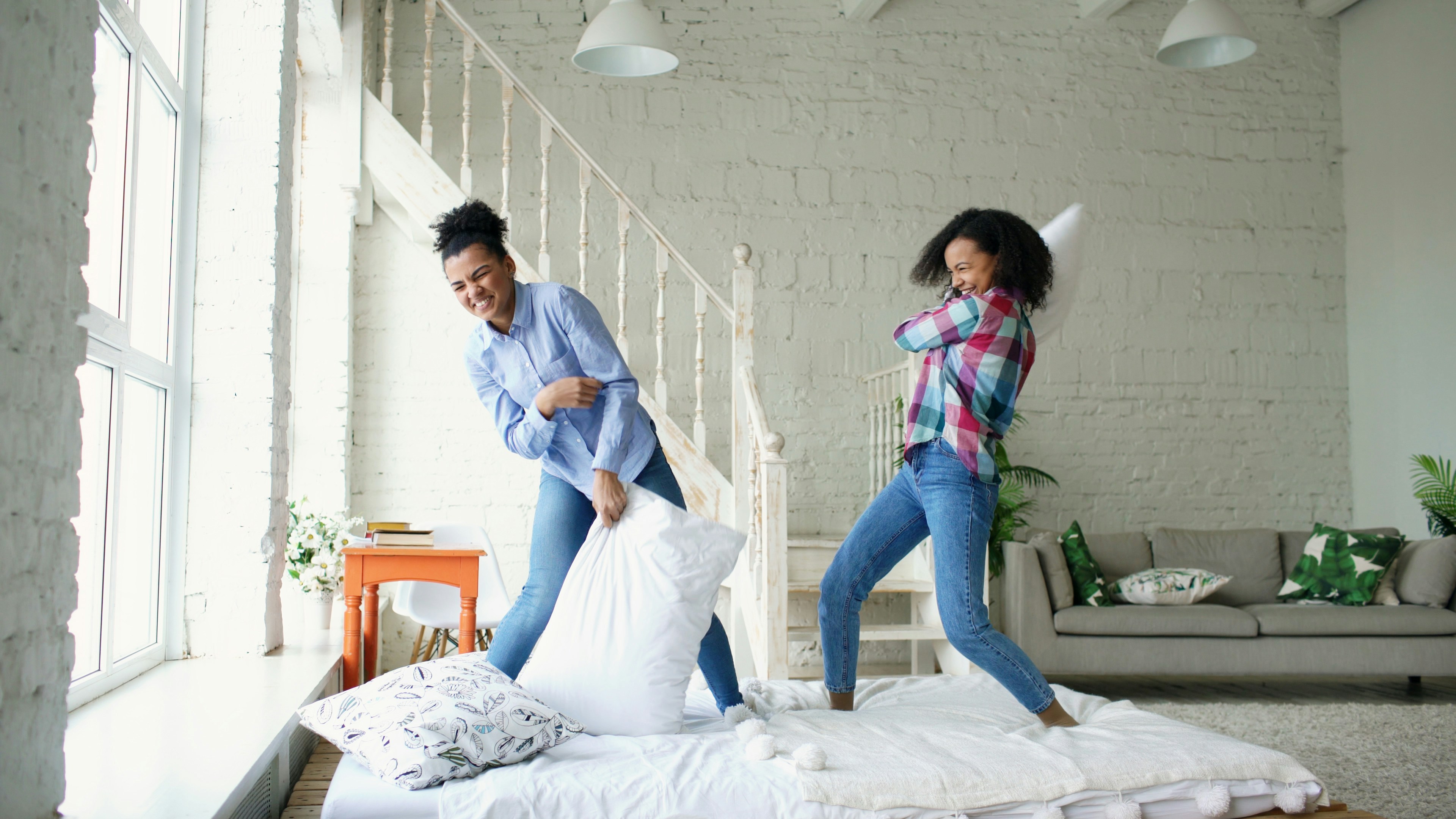 Two girls having a pillow fight on a bed.