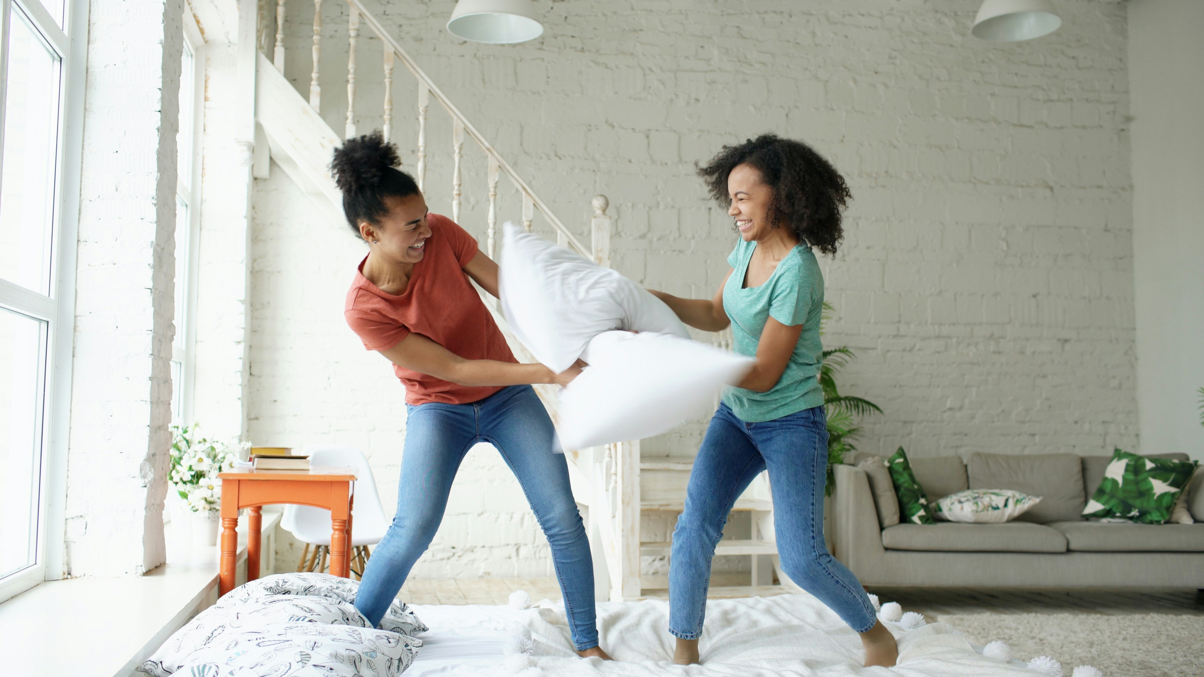 Two young women having a pillow fight indoors.