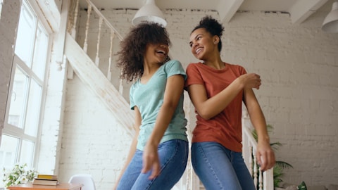 Two women dancing and laughing together indoors.