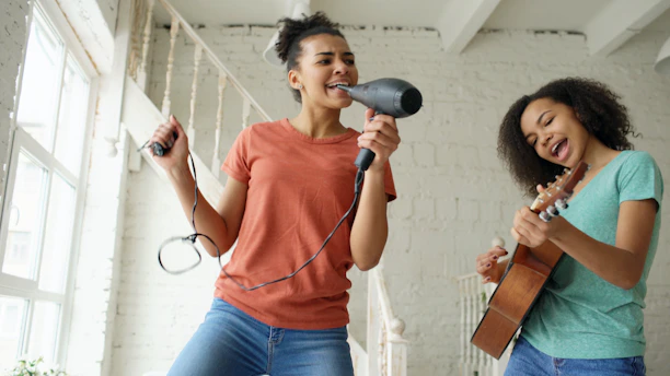 Two girls singing and playing guitar together indoors.