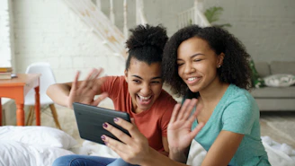 Two young women waving at a tablet
