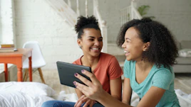 Two young women laughing while looking at a tablet.