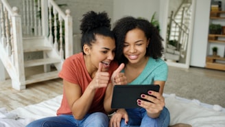 Two women smiling and giving thumbs up with tablet.