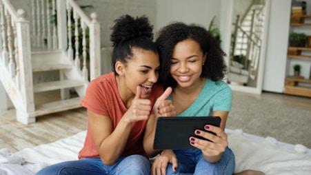 Two women smiling and giving thumbs up with tablet.