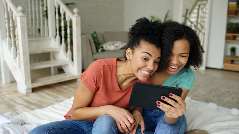 Two women laughing while looking at a tablet.