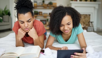 Two young women reading books and using tablet.