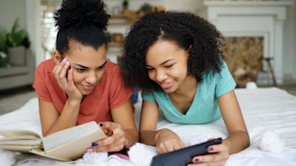 Two young women looking at a phone and book.