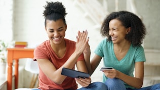 Two women high-fiving while looking at a tablet