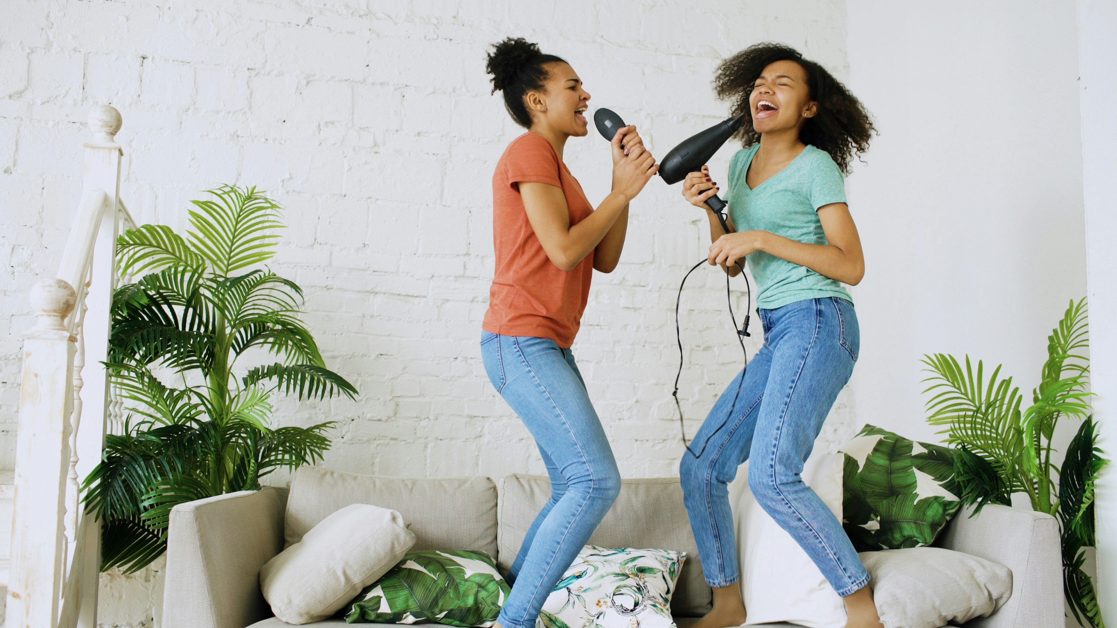 Two women jumping and singing with hair dryer and microphone