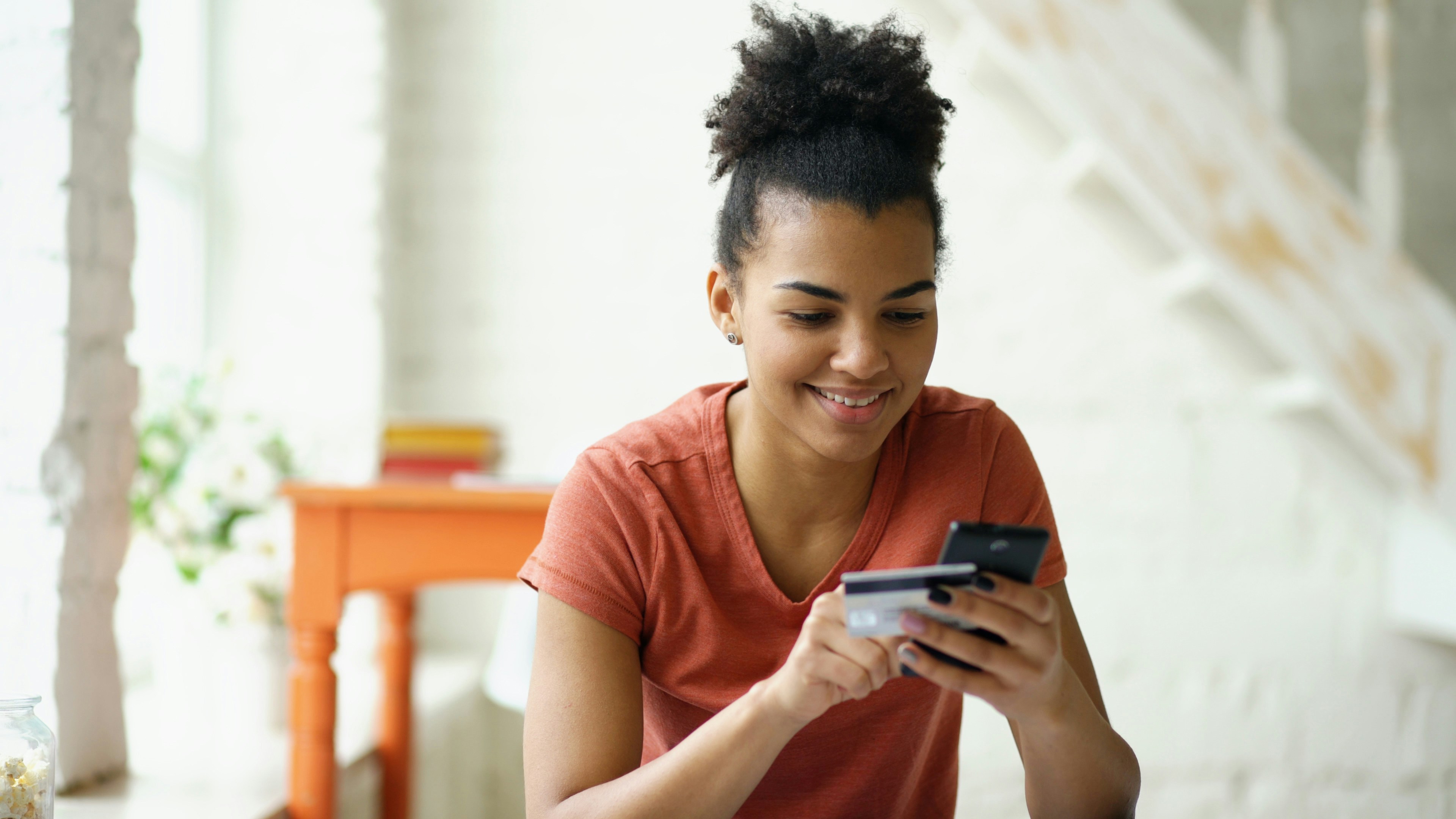 Beautiful happy mixed race woman online banking using smartphone shopping online with credit card at home