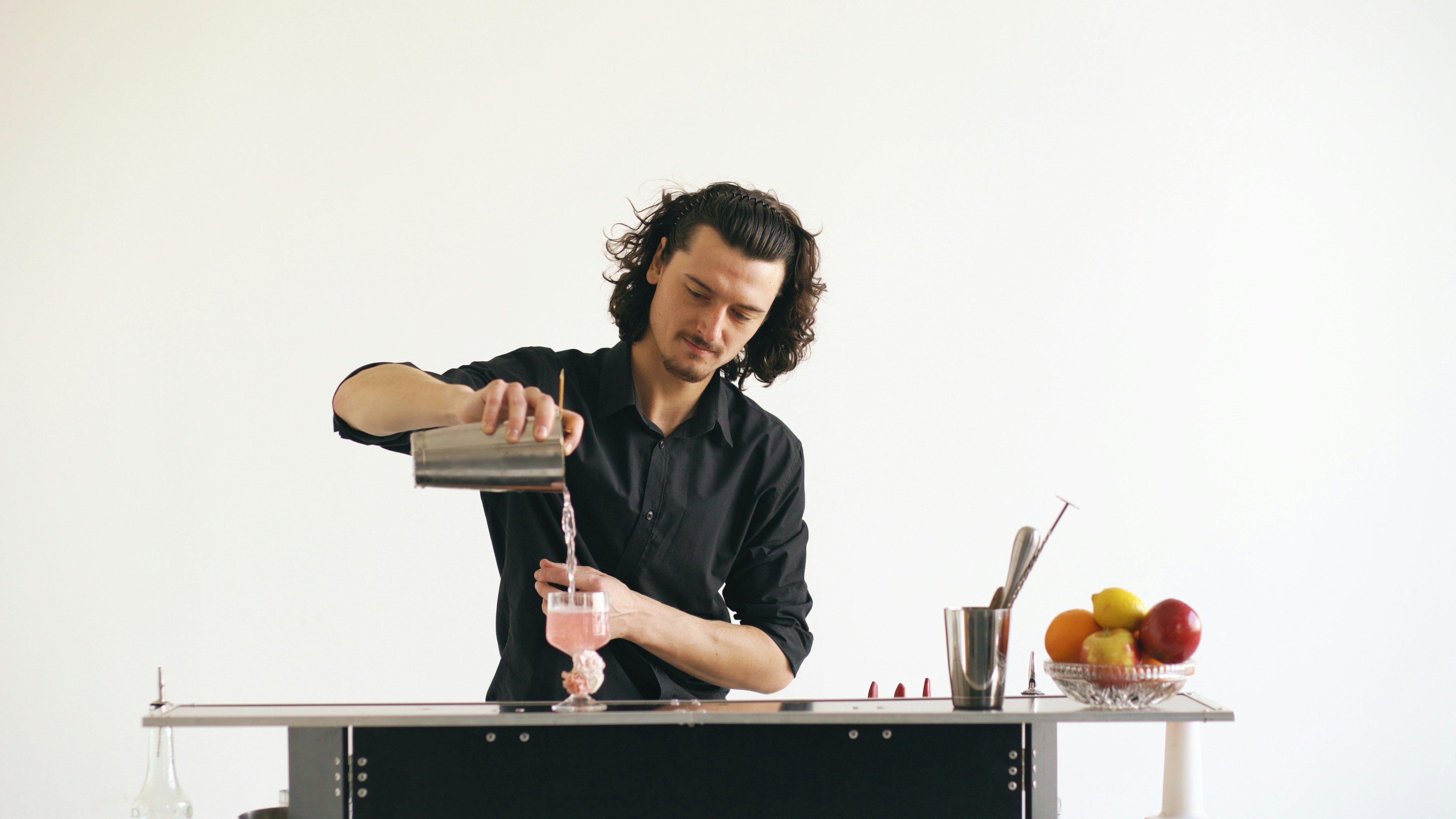 Bartender pouring pink cocktail into glass at bar.