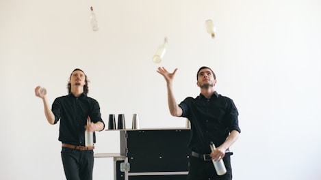Two bartenders juggling bottles against a white background.
