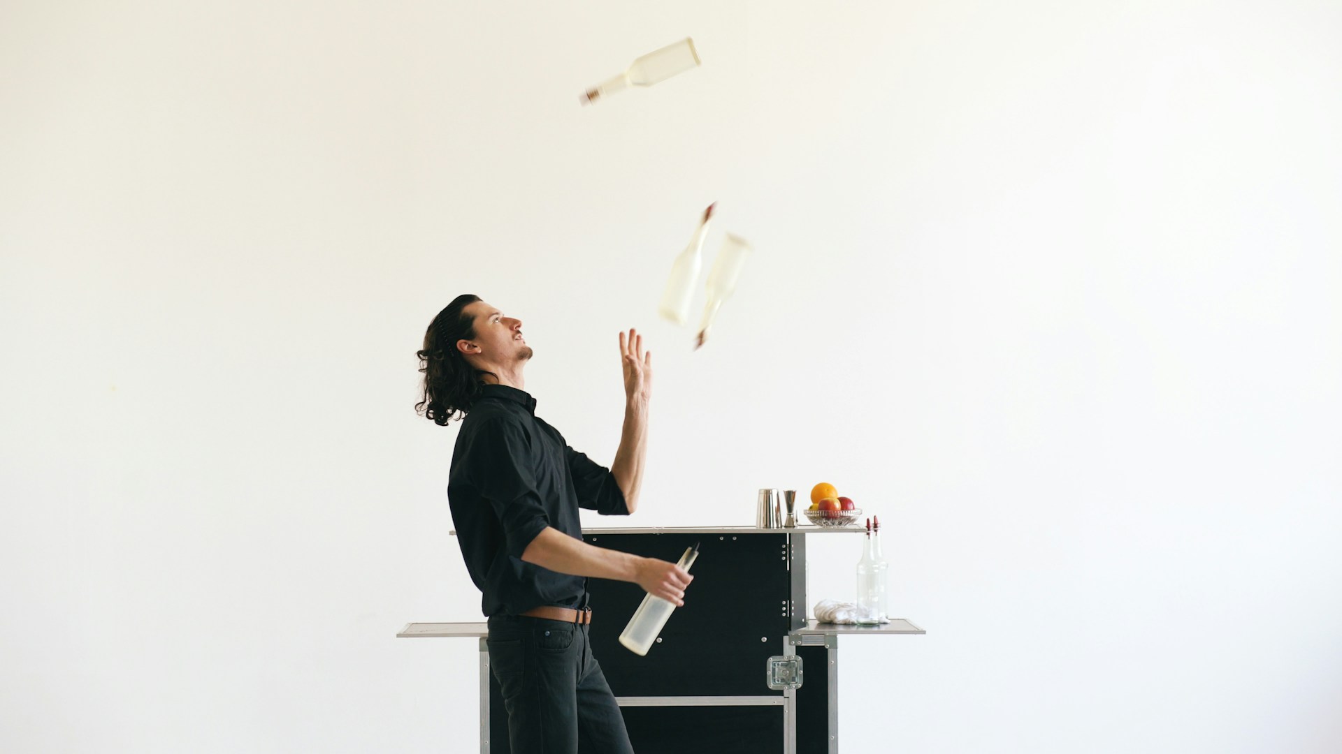 Bartender juggling bottles in a white room