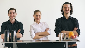 Three smiling bartenders standing behind a bar.