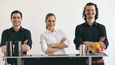 Three smiling bartenders standing behind a bar.
