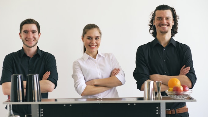 Three smiling bartenders standing behind a bar.