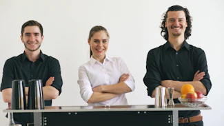 Three smiling bartenders standing behind a bar.