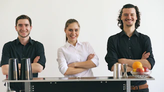 Three smiling bartenders standing behind a bar.