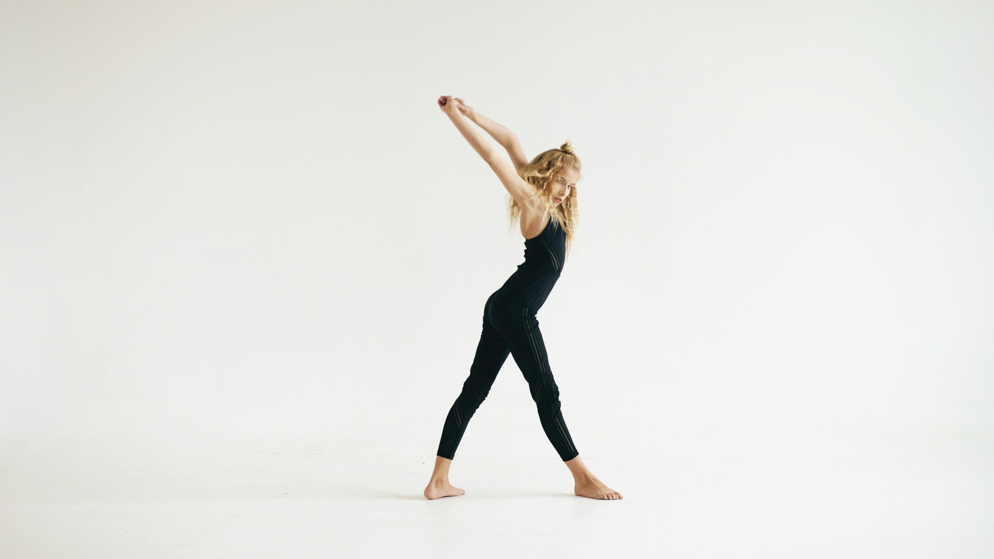 Young woman in black leotard stretching arms upward
