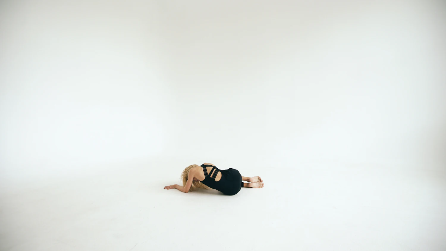One person lying curled on the floor in the middle of a very large empty pale room
