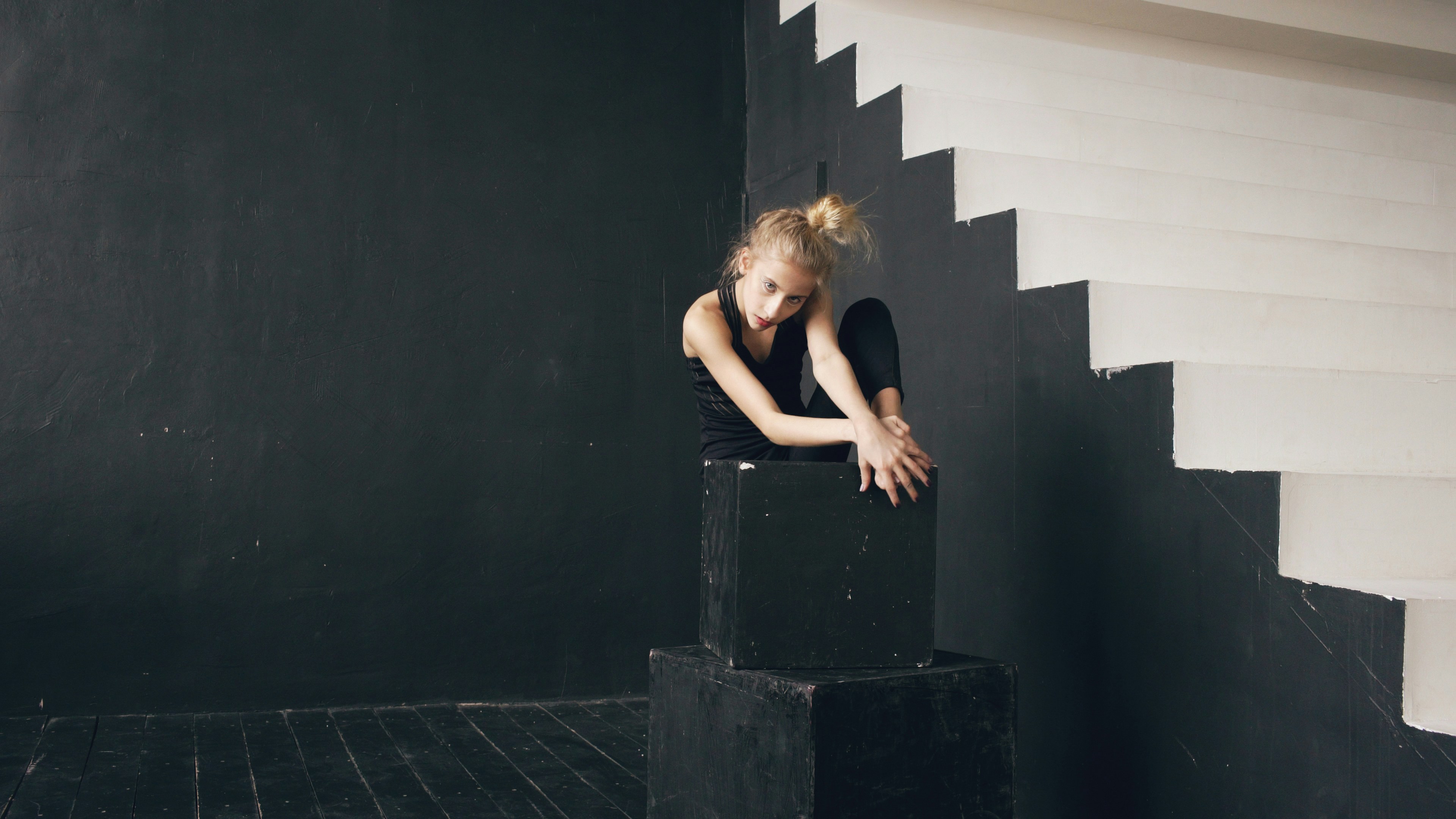 Young dancer poses on black cubes near stairs