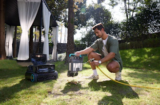 Man watering a robotic lawnmower in a garden.