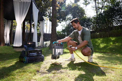Man watering a robotic lawnmower in a garden.