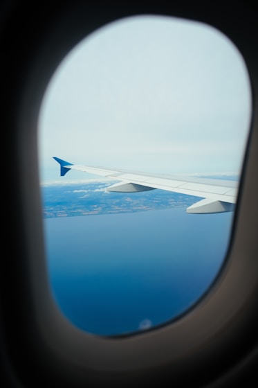 Airplane window view of wing over ocean and land.