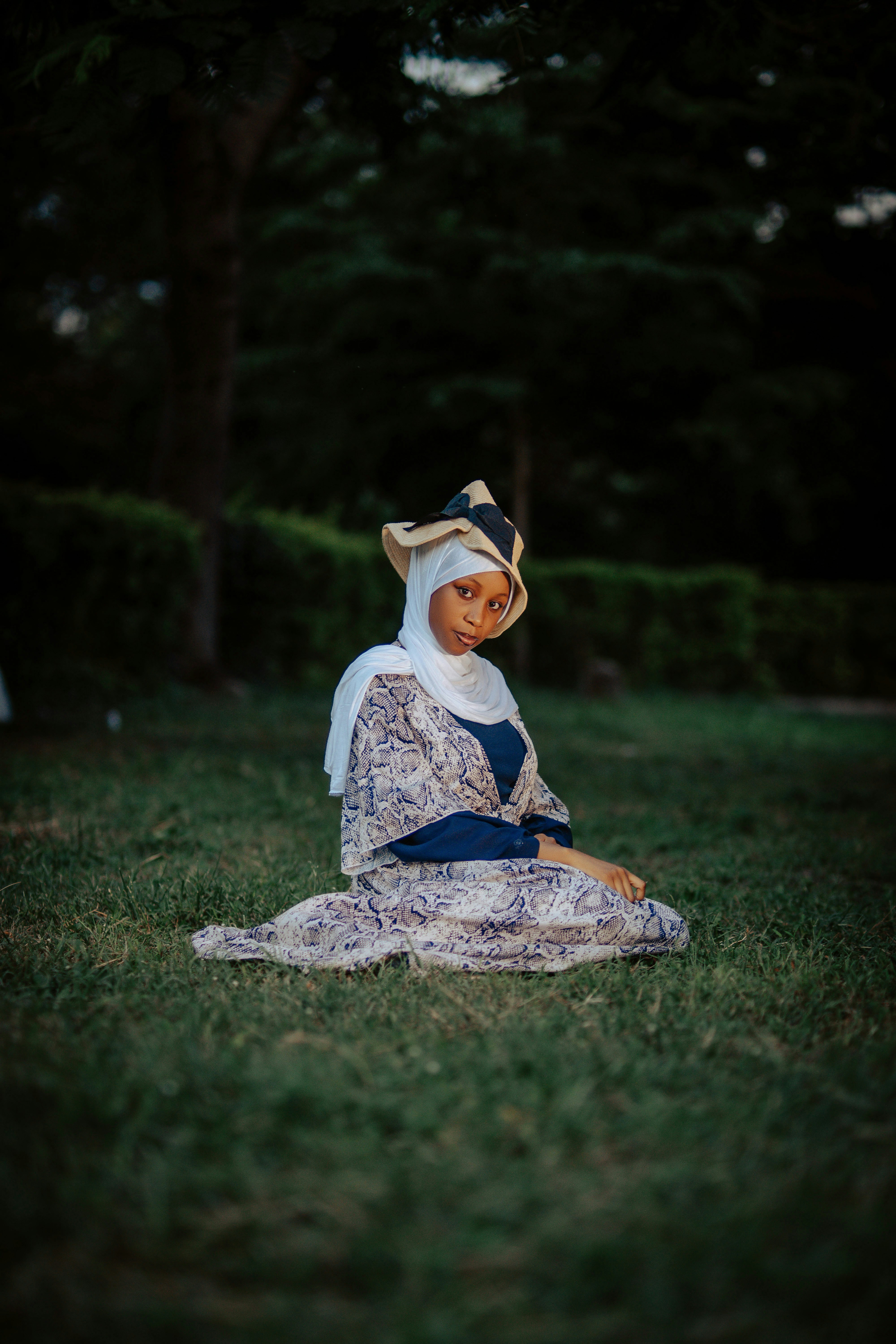 Wanita muda berjilbab dan topi duduk di atas rumput