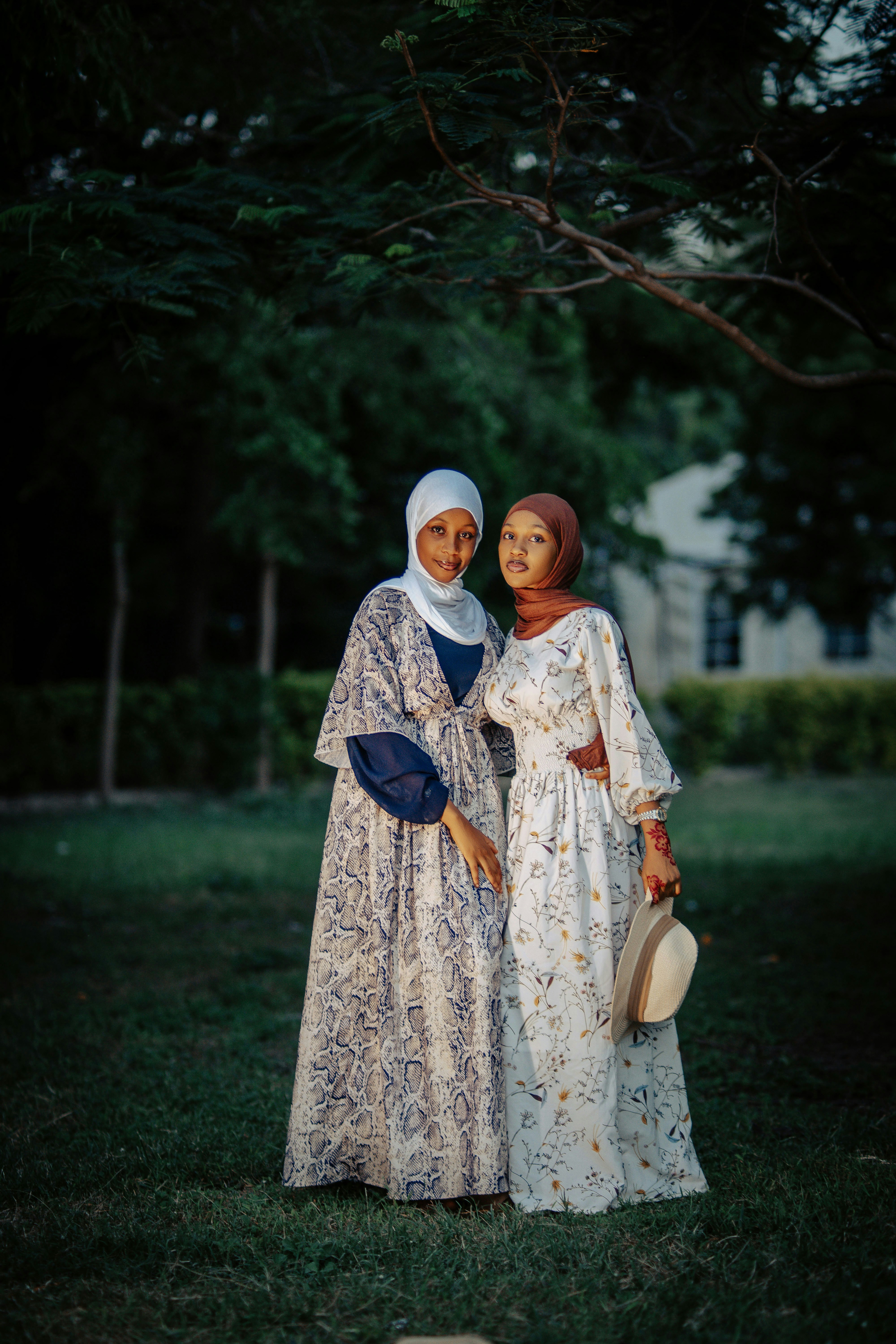Two women in hijabs and dresses pose outdoors.