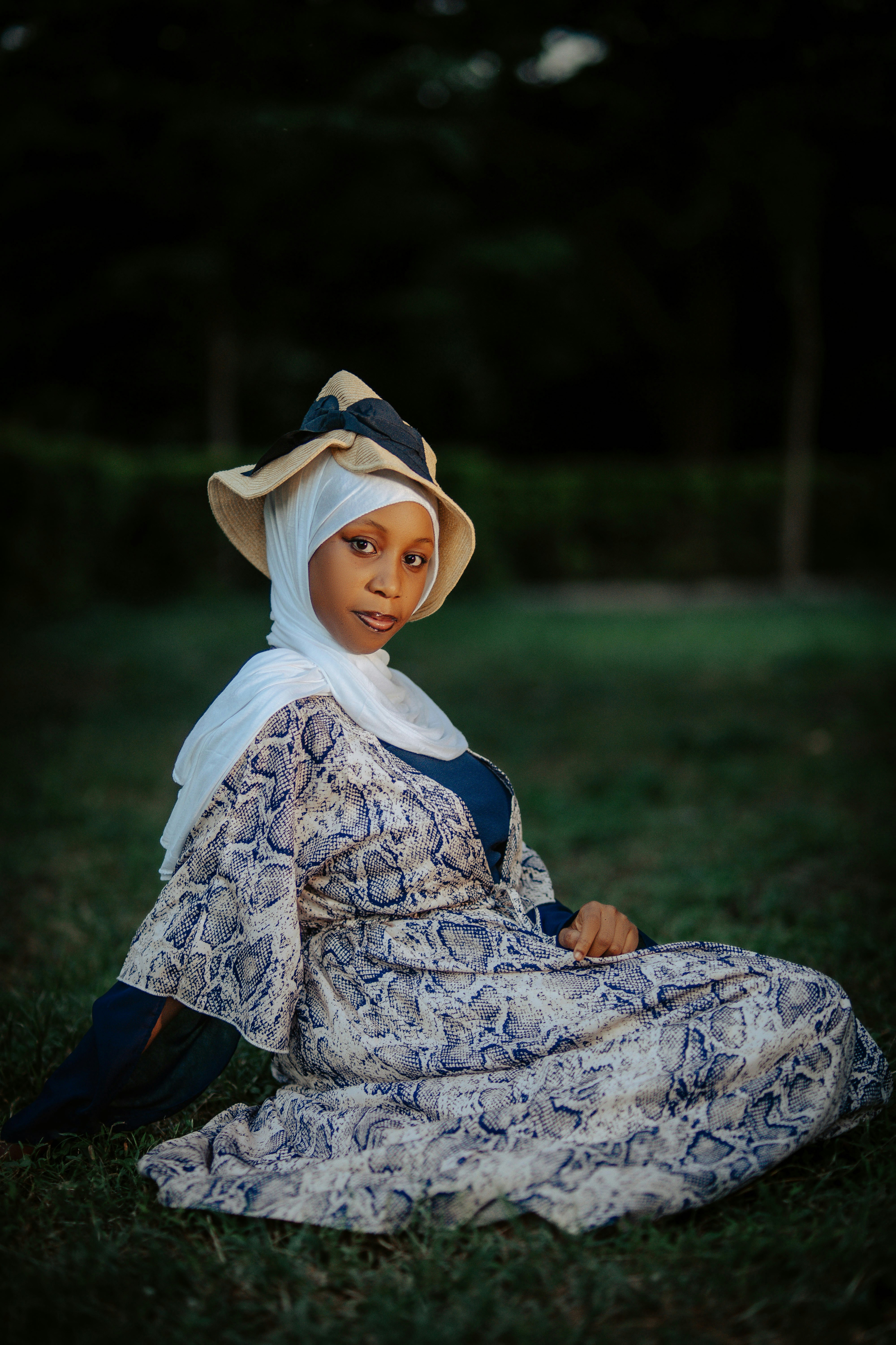 Wanita muda berjilbab dan topi duduk di atas rumput
