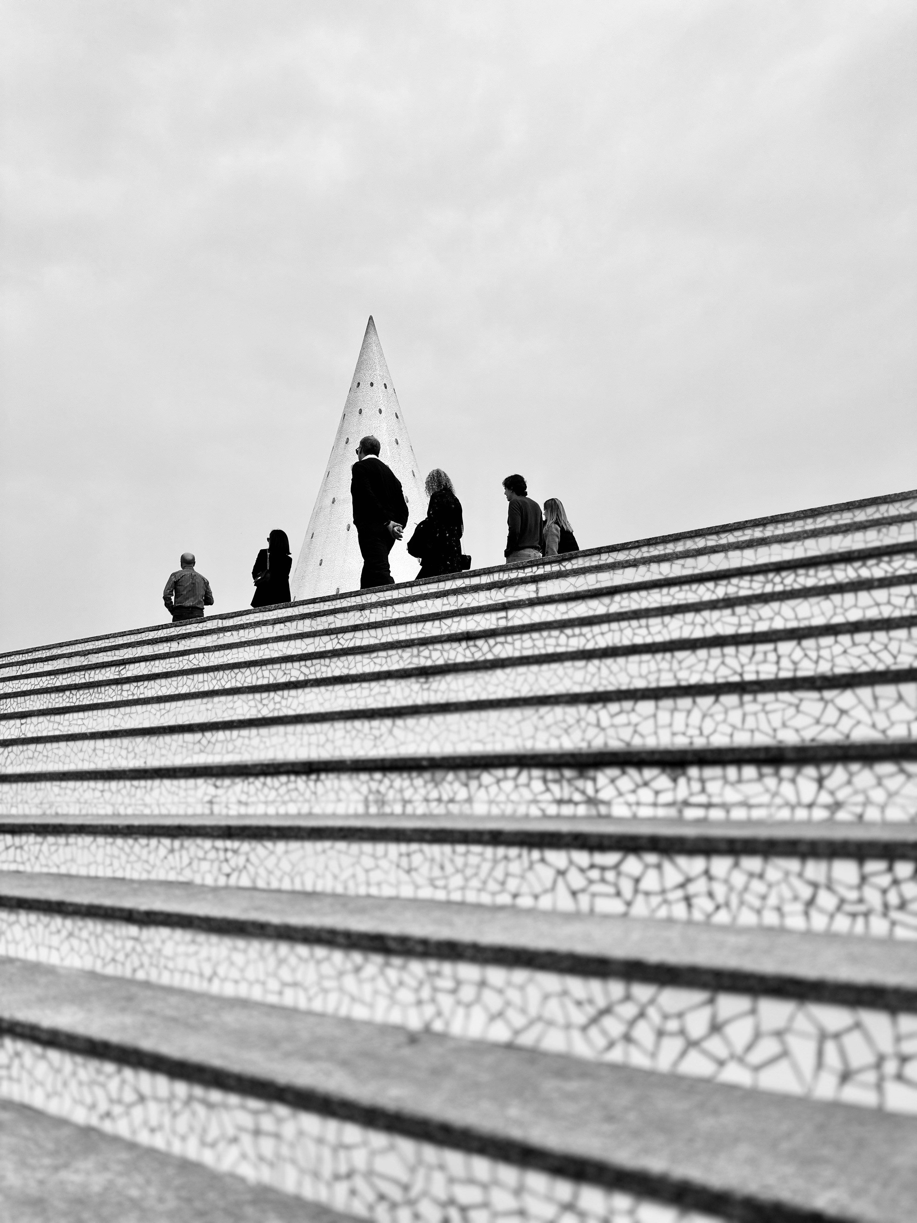 People gathered on mosaic stairs with conical structure.