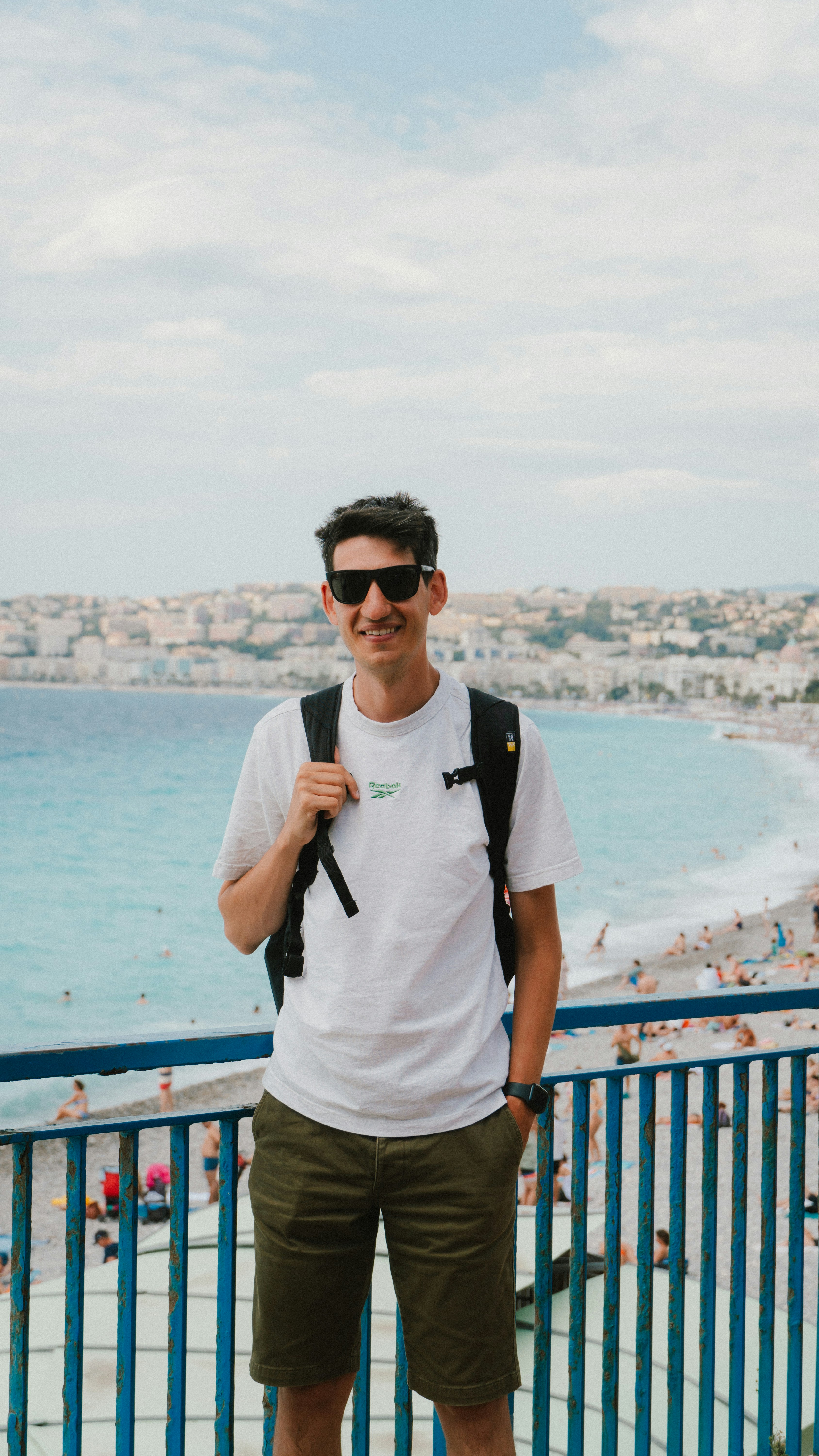 Man in sunglasses stands on a balcony overlooking beach.