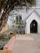 A quaint building entrance with a garden and arched doorway.