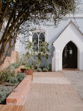 A quaint building entrance with a garden and arched doorway.