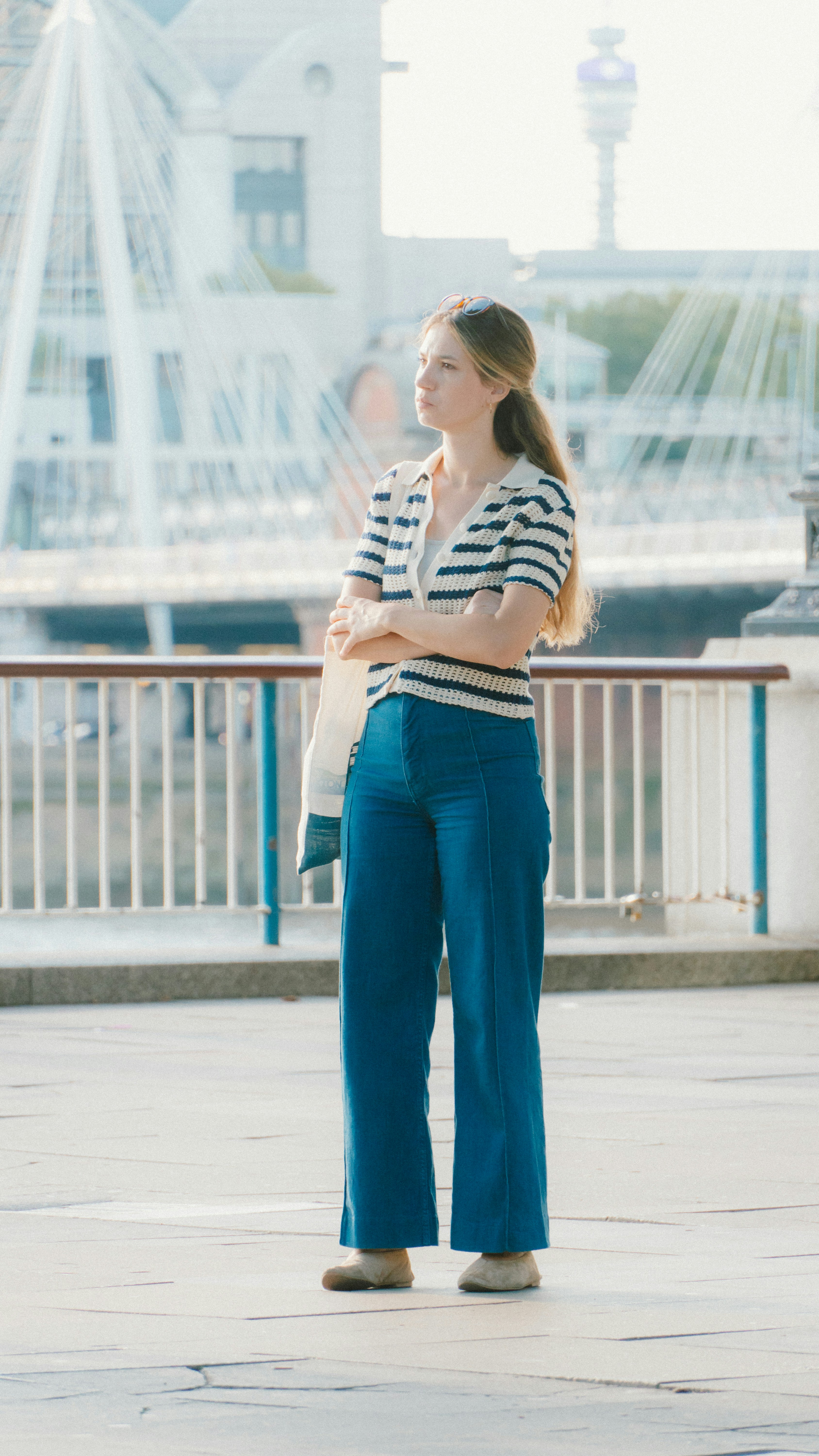 Woman in striped shirt and blue pants stands outdoors.