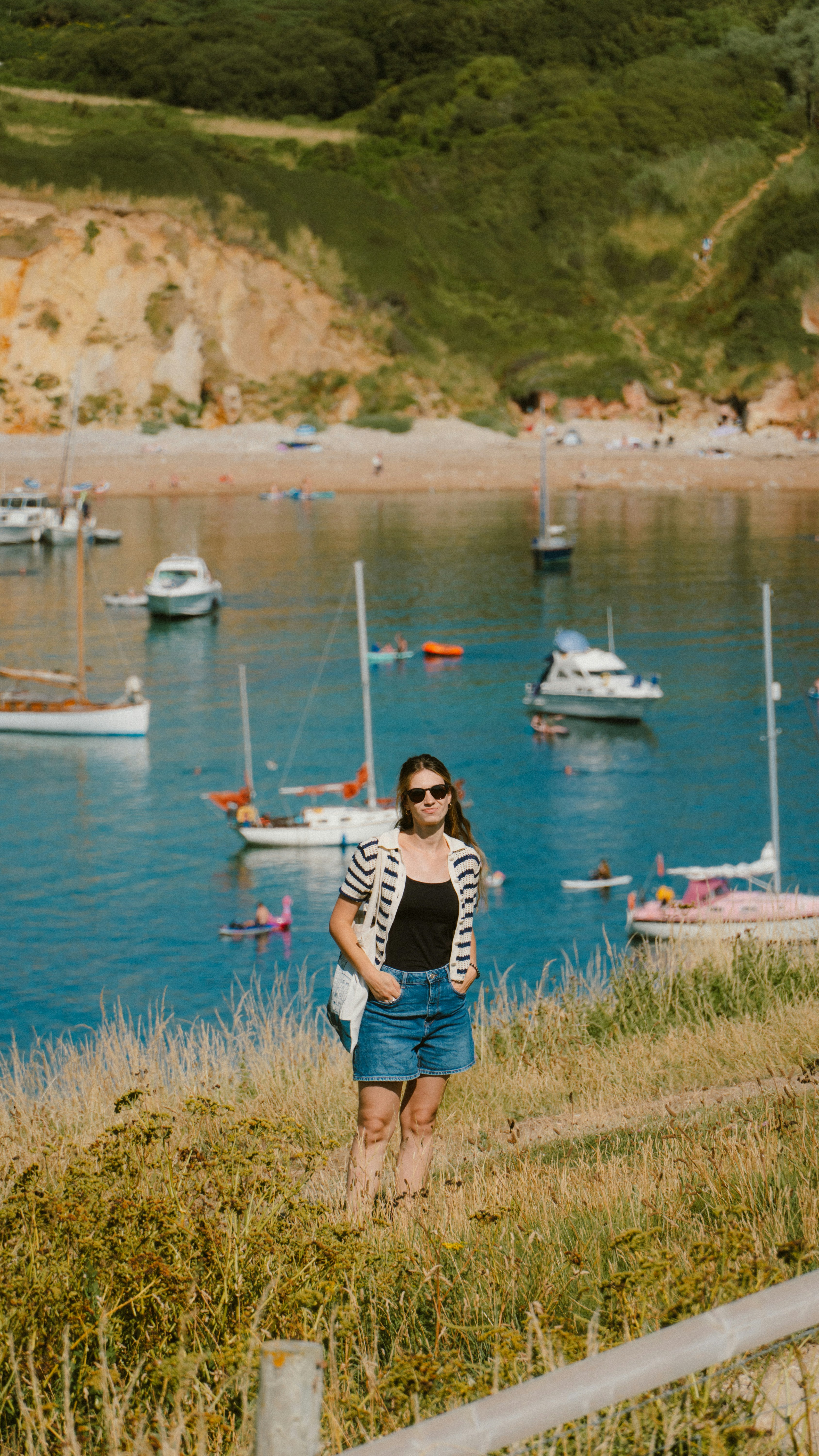 Young woman standing on grassy hill overlooking bay with boats.