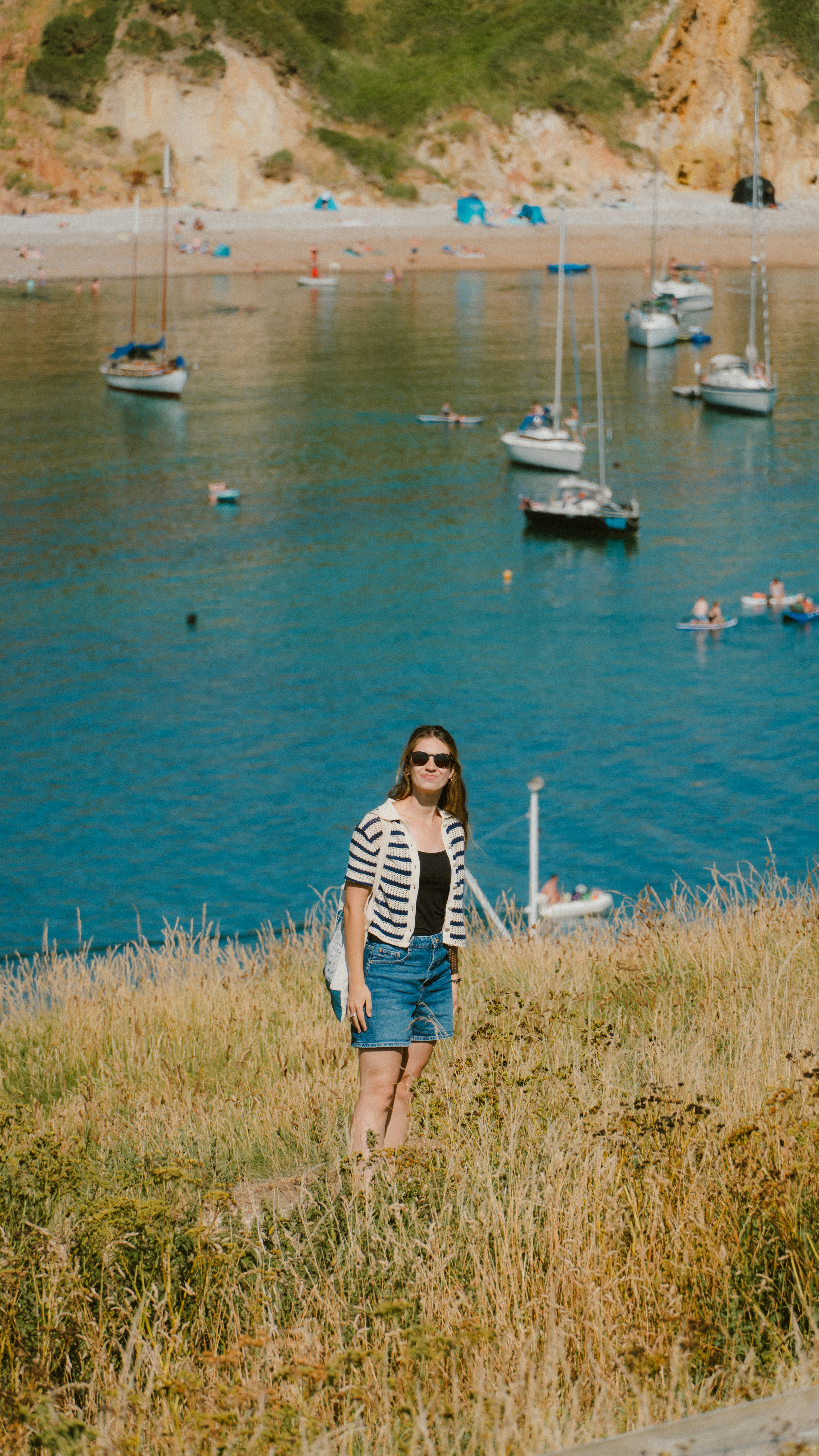 Woman standing on grassy hill overlooking bay with sailboats