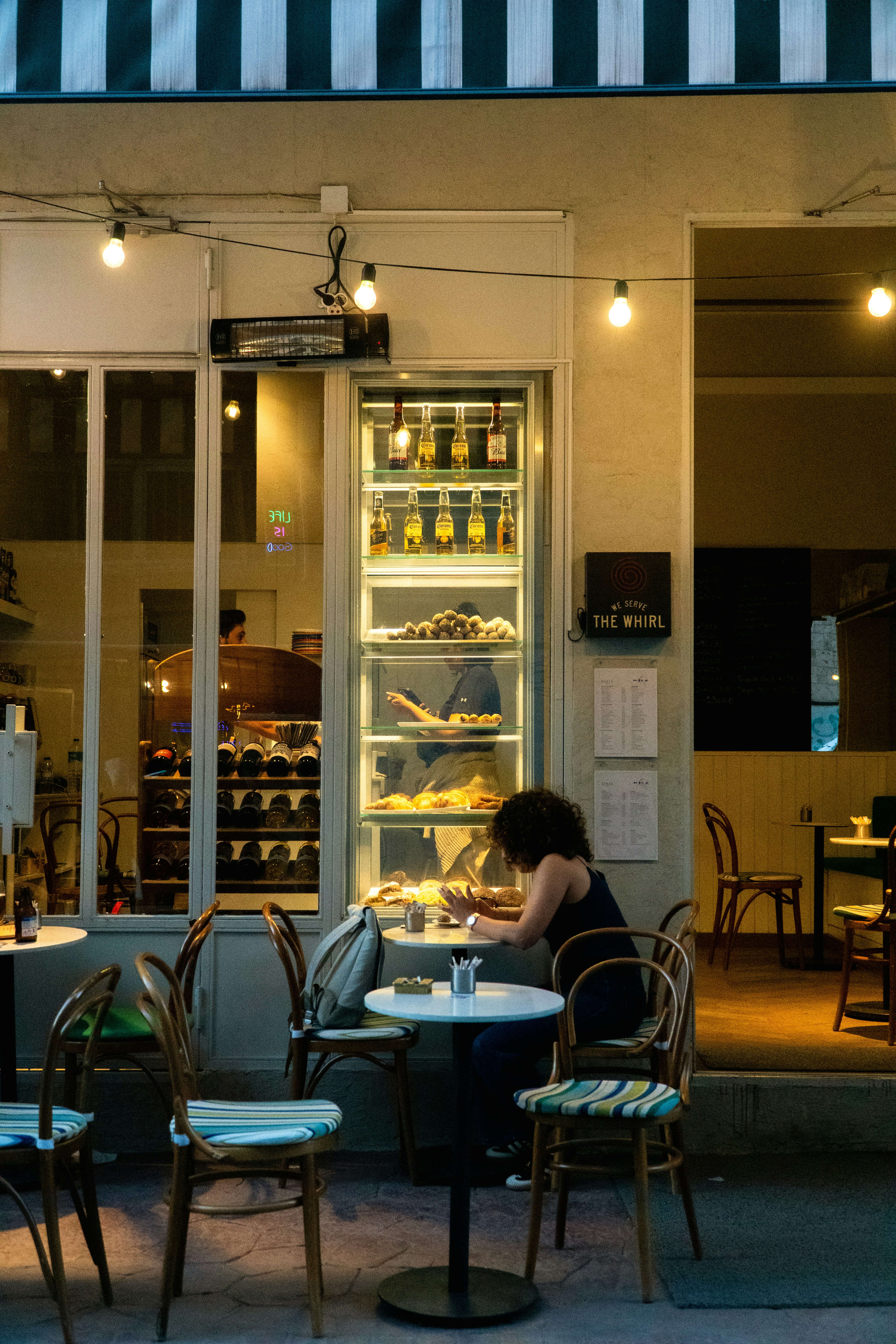 Woman sitting at table outside cafe at night.