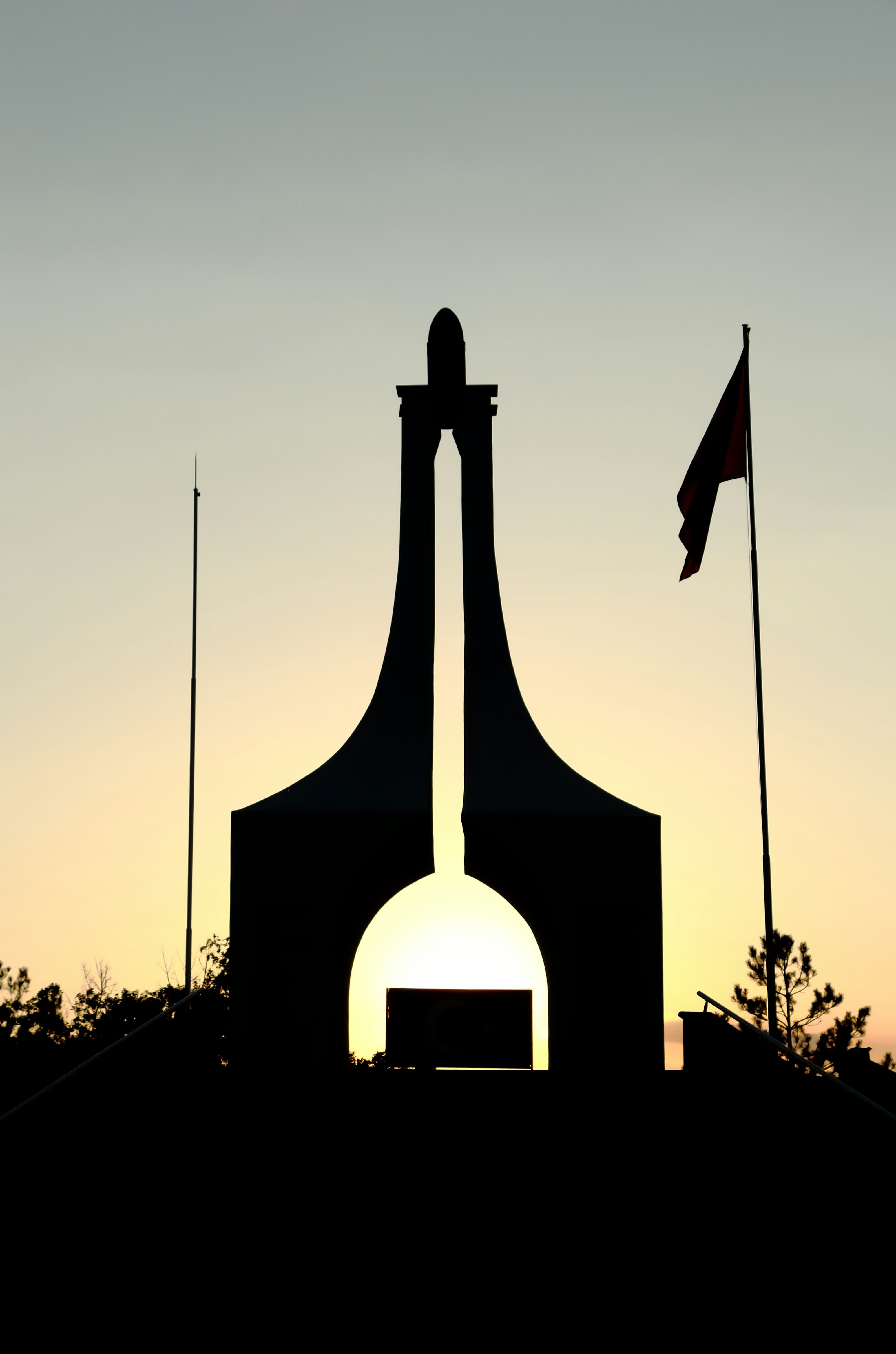 Monument silhouette against a sunset sky with flag.