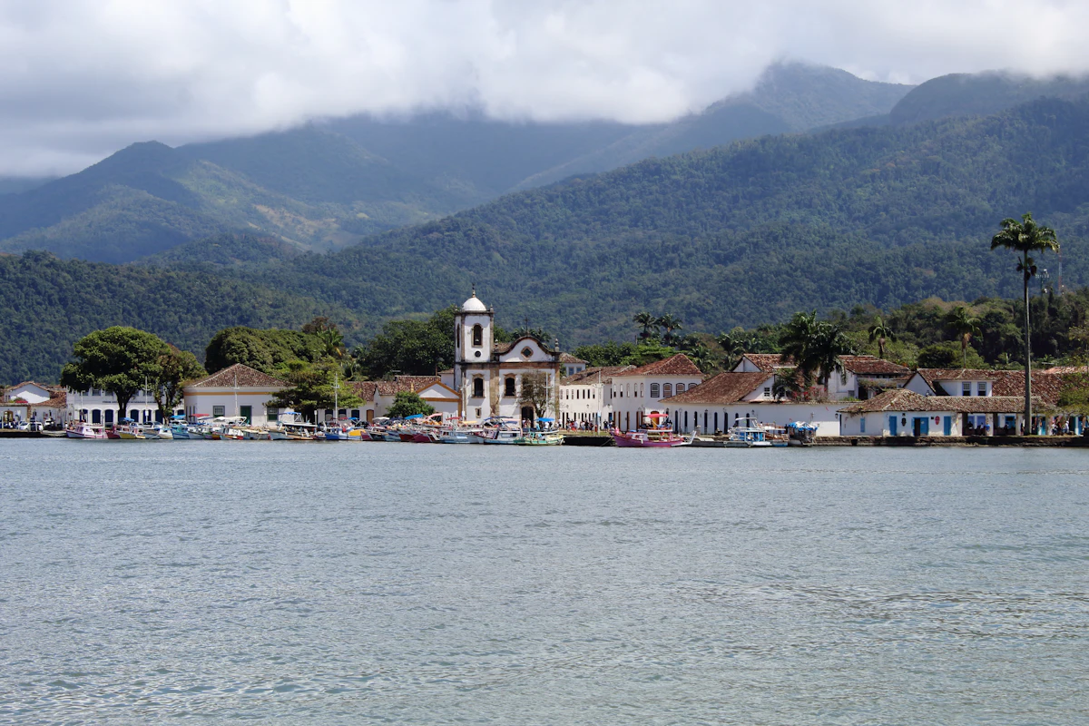 Paraty's waterfront, with a white church and colonial houses below forested mountains in cloud