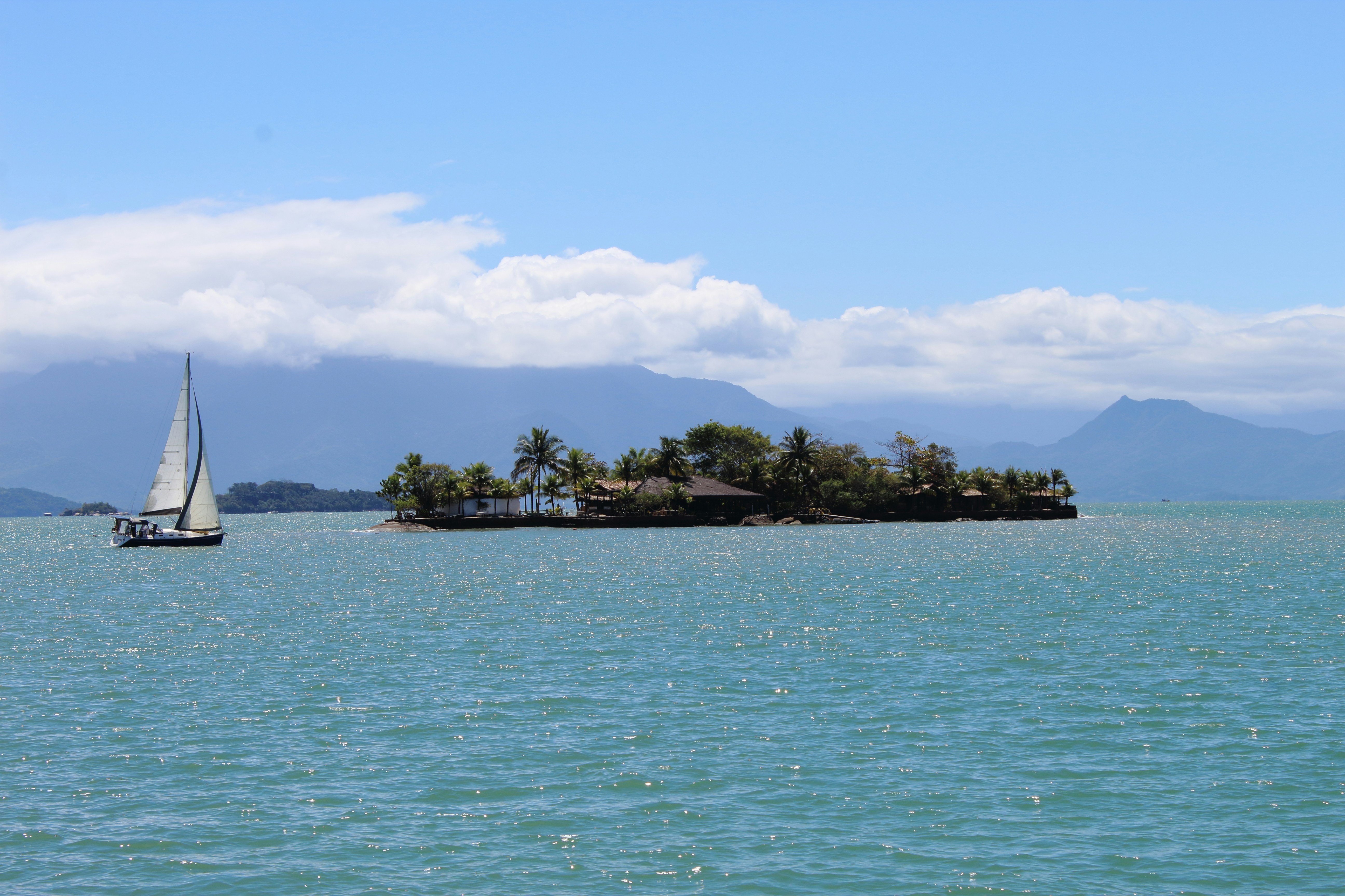 Un voilier s’approche d’une île tropicale avec des montagnes derrière.