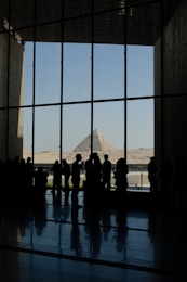 Silhouettes of people looking at pyramids through a large window.