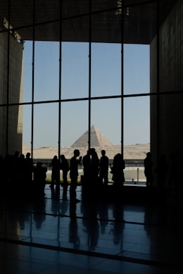 Silhouettes of people looking at pyramids through a large window.