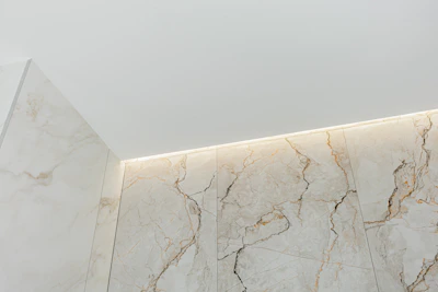 Modern bathroom corner with marble walls and ceiling light.