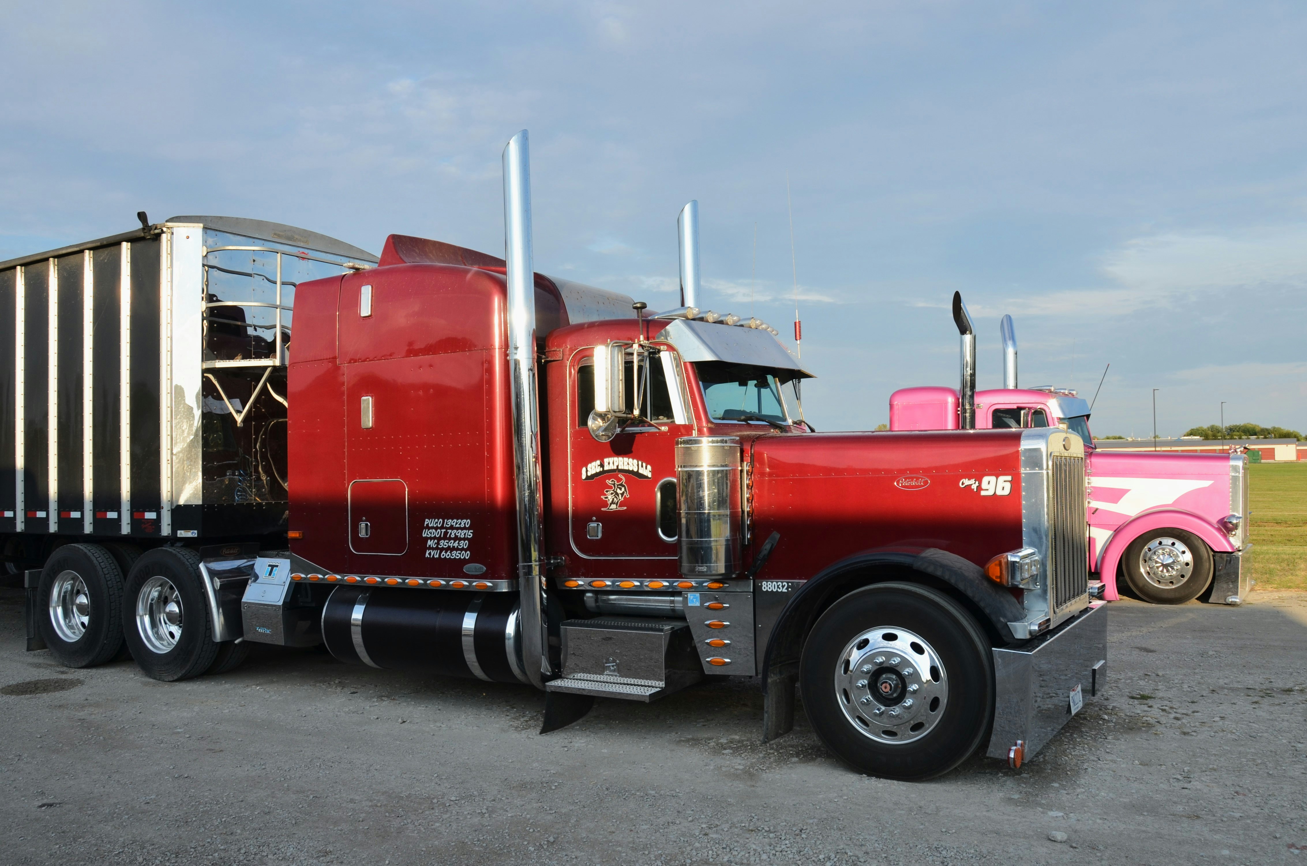 Two semi-trucks, one red and one pink, parked.