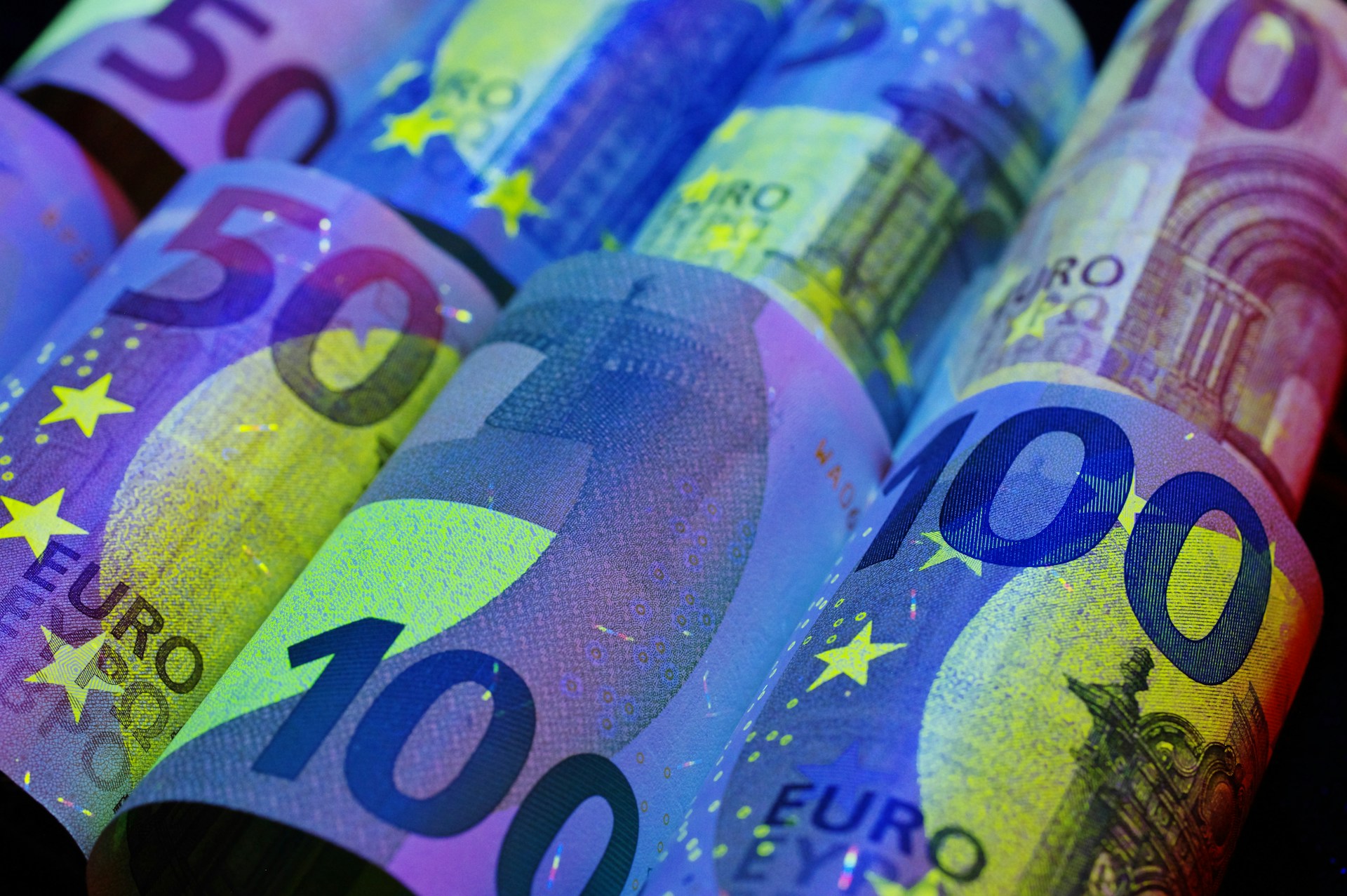 Rolled euro banknotes illuminated under ultraviolet light.