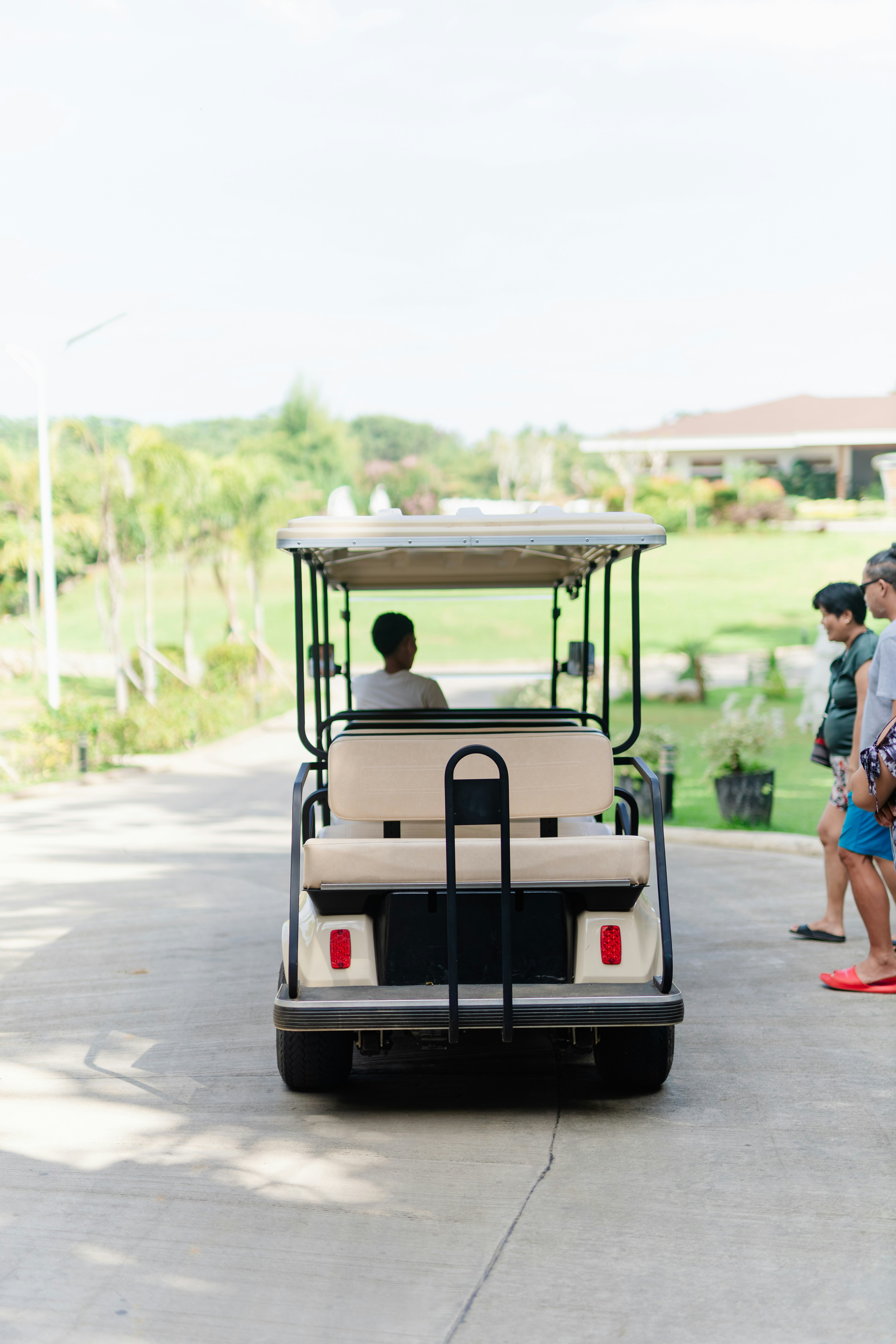 Golfwagen mit Fahrer und Beifahrern auf asphaltiertem Weg.